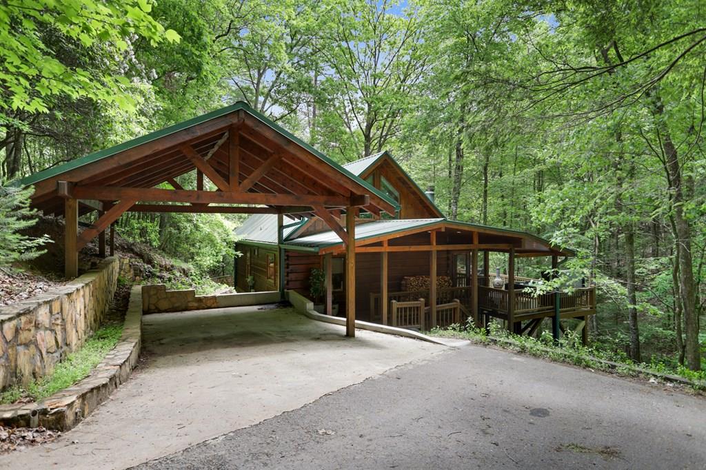 Rustic wooden cabin in a lush green forest with a covered carport and front porch.