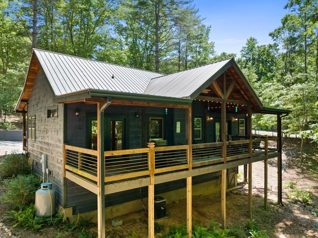 Wood cabin on stilts with a wraparound porch in a forested setting, metal roof and string lights.