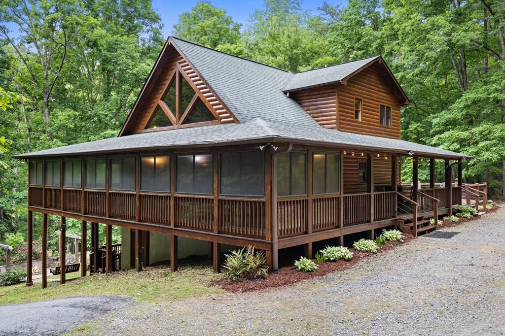 Wooden screened-in cabin on stilts in a forest, with a long wraparound porch and peaked roof.