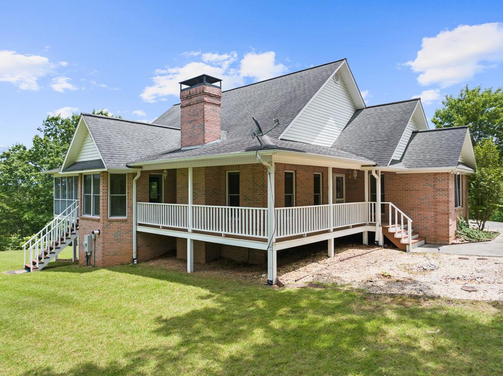 Brick house with a wraparound white railing porch, brick chimney, and a manicured lawn under a bright blue sky.